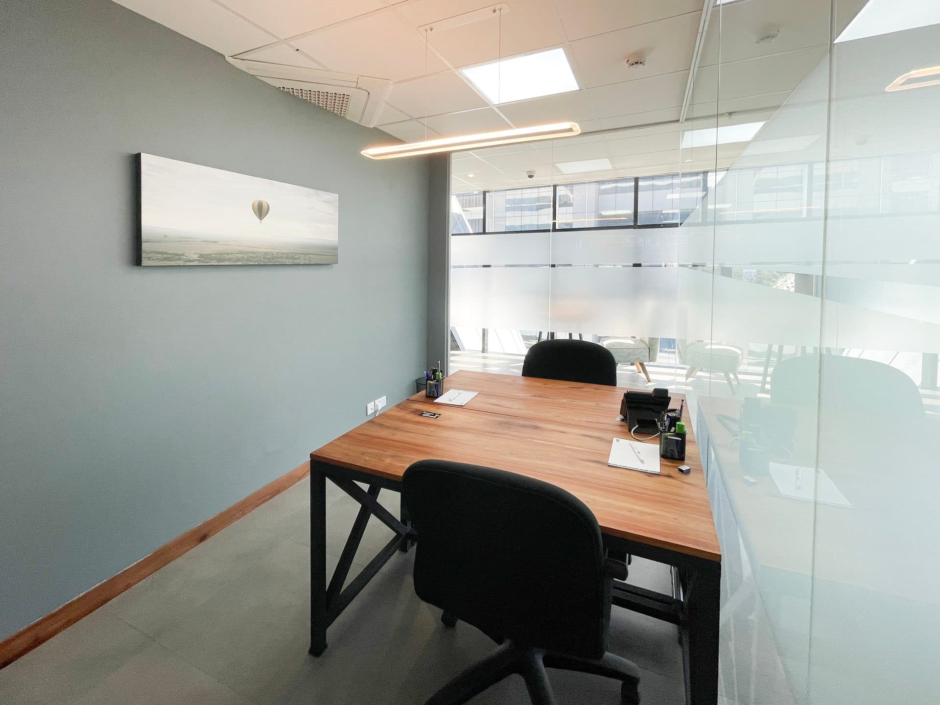 A single-person office at ZO Premium with a painting on the wall and a glazed partition