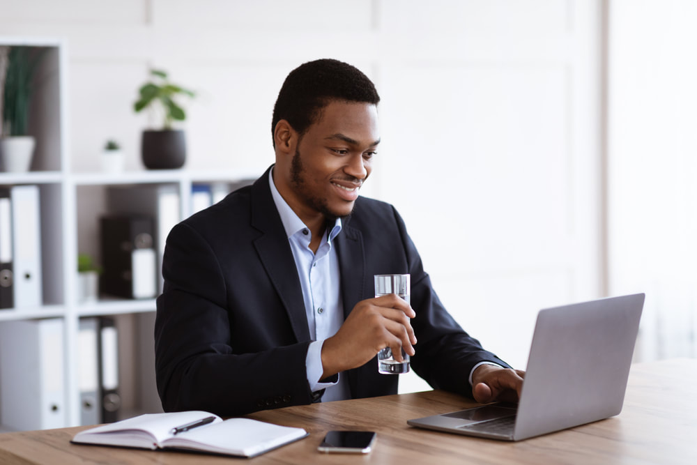 A smiling man seated in a modern and well-furnished office space. The office features high-speed internet, comfortable furniture, and all the essential elements that contribute to a productive and pleasant work environment. 