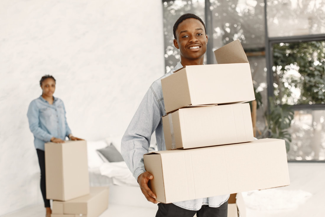 A confident black man in professional attire, holding a stack of moving boxes, ready to facilitate an office relocation with efficiency and expertise.